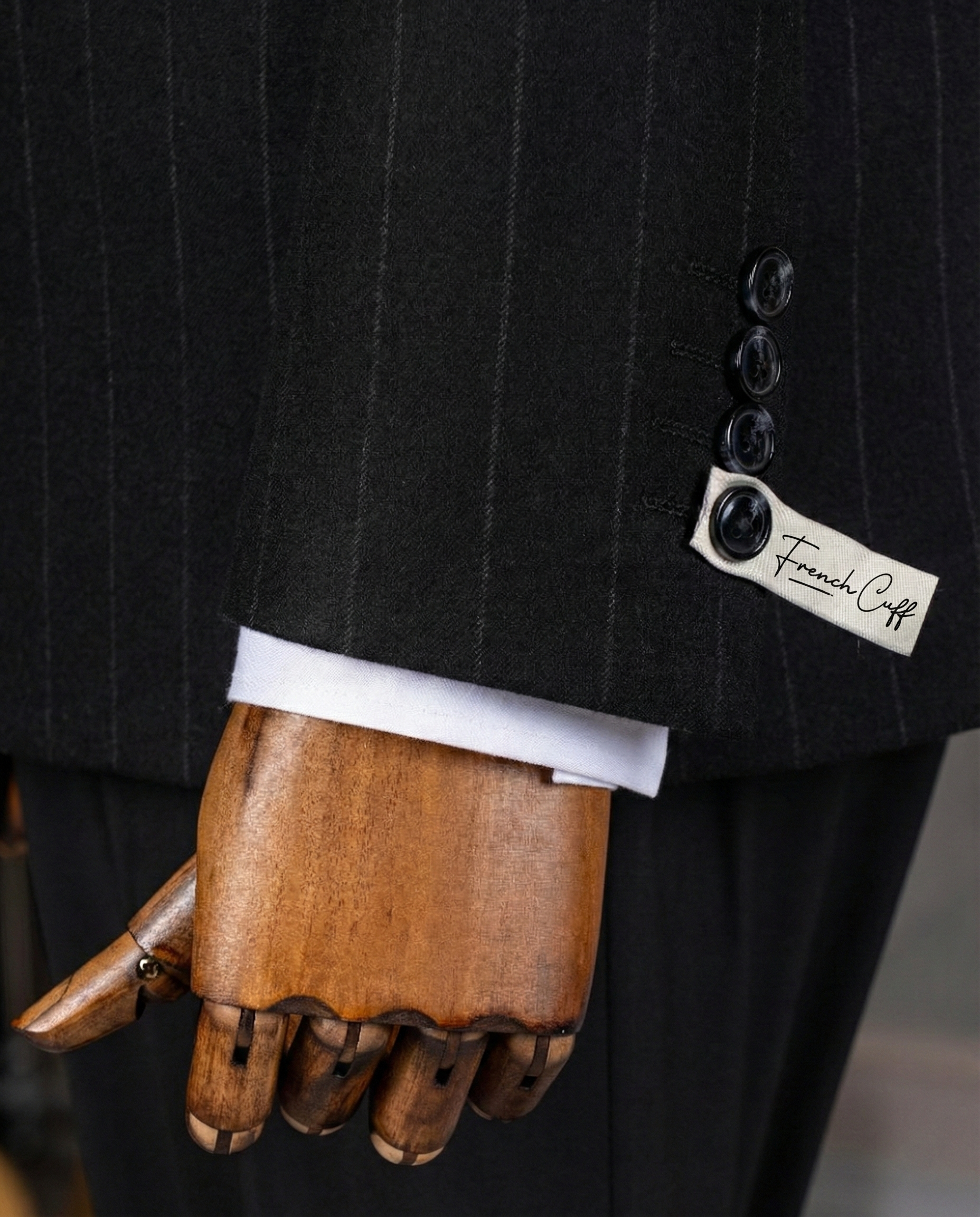 Close-up of a black pinstripe suit with a wooden hand wearing a white shirt cuff, featuring a 'French Cuff' label.